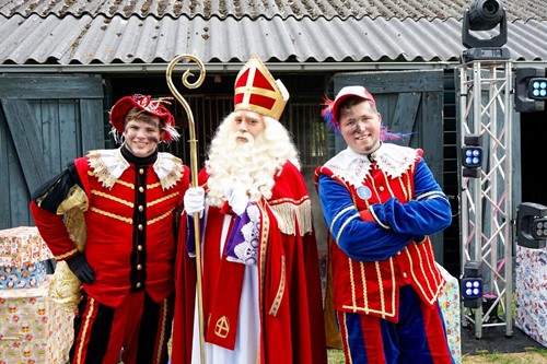Sinterklaas samen met twee pieten in rood en blauw kostuum tijdens het feest.