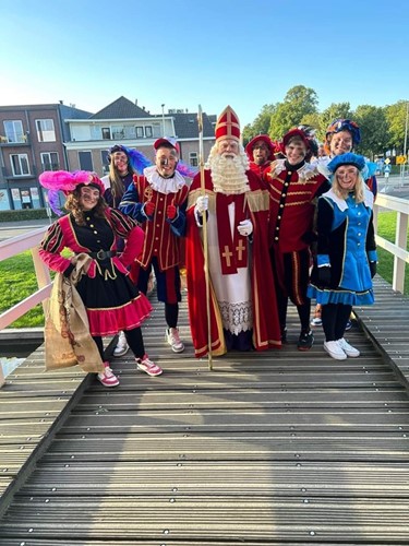 Groepsfoto van Sinterklaas met meerdere pieten in kleurrijke kostuums op een brug.